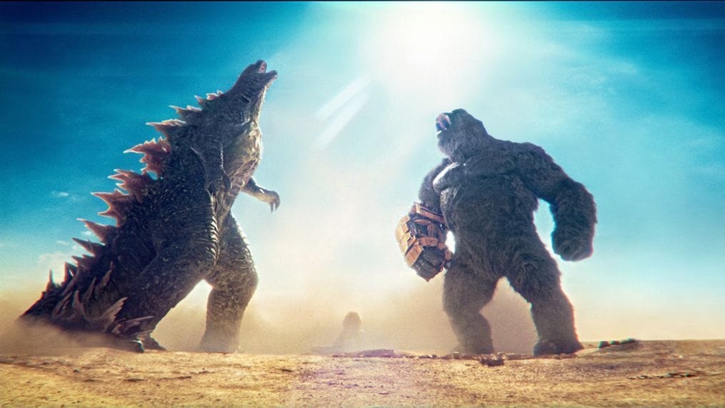 A large mutated lizard and an oversized gorilla wearing an arm brace face each other and roar against a bright blue sky.