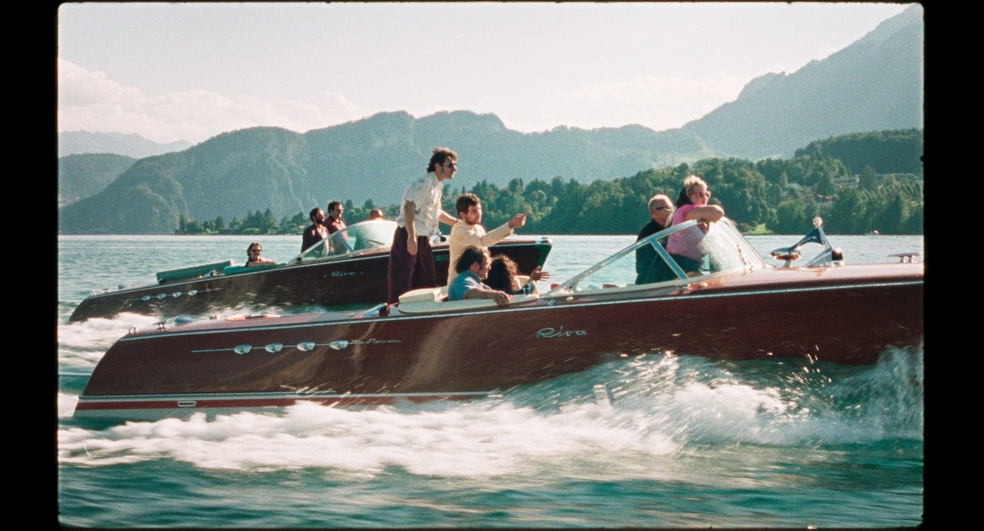 A group of primarily white people in their 20s and 30s ride two speedboats in a lake.